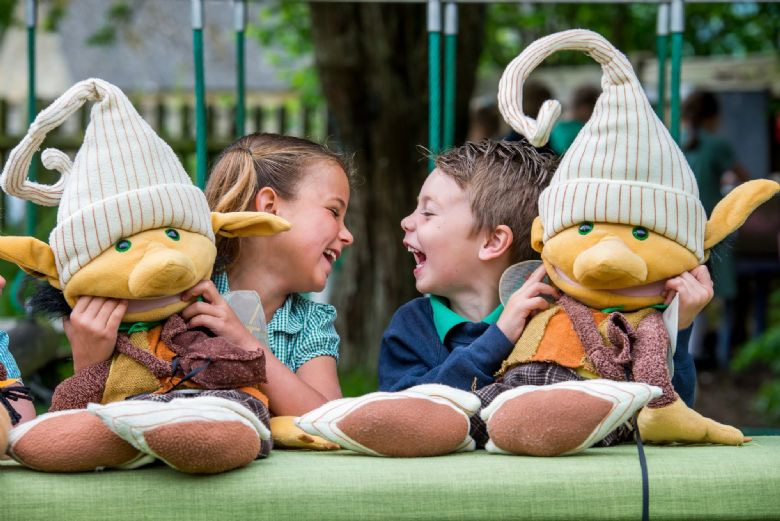 Two primary school children holding elf cuddly toys, laughing.